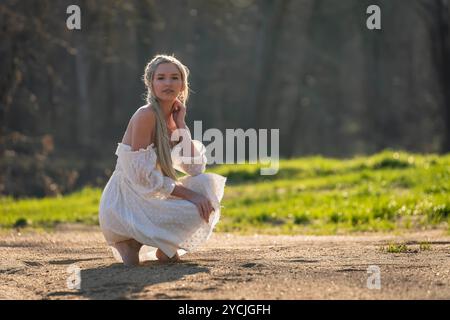 Eine atemberaubende junge Frau geht an einem Bach vorbei, ihr weißes Frühlingskleid schwingt anmutig im Wind. Umgeben von üppigen Wäldern, genießt sie die Ruhe Stockfoto