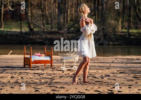 Eine atemberaubende junge Frau geht an einem Bach vorbei, ihr weißes Frühlingskleid schwingt anmutig im Wind. Umgeben von üppigen Wäldern, genießt sie die Ruhe Stockfoto