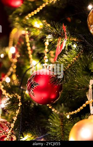 Aus nächster Nähe sehen Sie einen Weihnachtsbaum mit glitzernden Lichtern, roten Ornamenten und goldenen Girlanden, die einen festlichen und fröhlichen Feiertagsgeist hervorrufen. Stockfoto