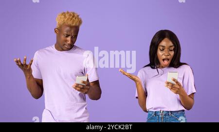 Schockierte schwarze Dame und Afroamerikaner, der in Smartphones auf violettem Hintergrund schaut Stockfoto