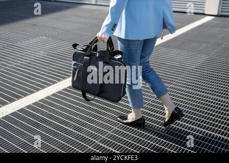 Geschäftsfrau läuft in einer urbanen Umgebung, trägt eine Aktentasche und trägt einen blauen Blazer und Jeans Stockfoto