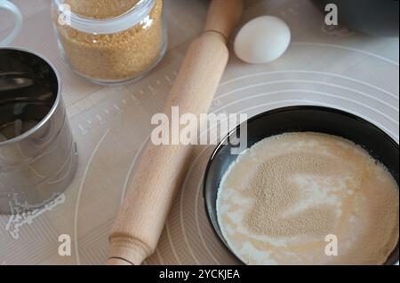 Close-up-Backzutaten zum Backen von süßen Brötchen, Hefe und Milch in schwarzen Schüsseln, Pin auf einem Tisch Stockfoto