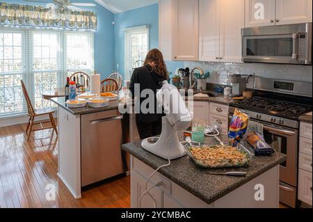 Frau in der Küche, die Thanksgiving-Mahlzeit zubereitete. Mehrere Beilagen stehen für den Ofen bereit. Stockfoto