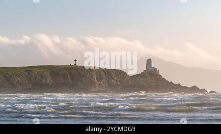 Der TWR Mawr Lighthouse und das St. Dwynwen's Cross sind an einem trüben, stürmischen Nachmittag an den exponierten Flanken von Llanddwyn Island hervorzuheben. Stockfoto