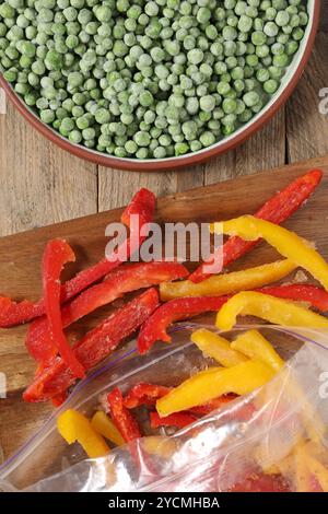 Gefrorene grüne Erbsen in der Schüssel und Paprika auf Holztisch, Blick von oben Stockfoto