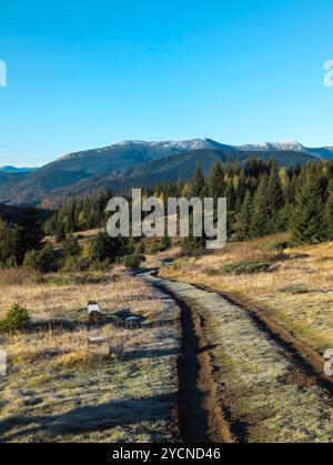 Mountain Path: Eine kurvige Schotterstraße führt durch eine malerische Landschaft mit schneebedeckten Bergen in der Ferne. Stockfoto