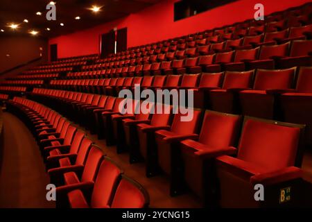 Rote Stühle stehen in einem Theater, der erste auf der rechten Seite und die anderen in einer Art unendlicher Reihenfolge nach links. Stockfoto