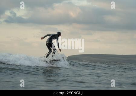 Ein junger Mann in einem schwarzen Neoprenanzug reitet auf einem Tragflächenboot-Surfbrett in kleinen Wellen vor dem Strand von Bourenmouth. Stockfoto