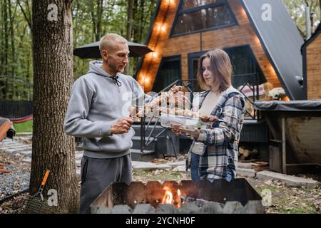 Ein Paar bereitet Spieße für das Grillen über offenem Feuer in der Kabine vor und genießt gemeinsam im Herbst das Grillen Stockfoto