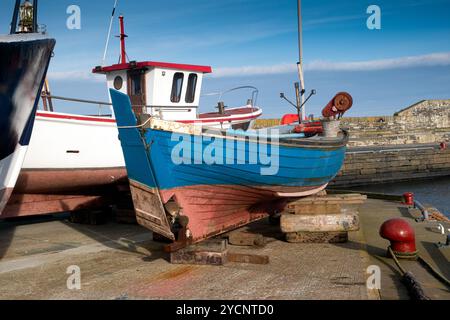 Farbenfrohe Fischerboote stiegen aus dem Wasser und ruhten auf Blöcken am Wick Harbour Stockfoto