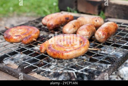 Leckere Würstchen über glühende Kohlen auf dem Grill Feuer kochen Stockfoto