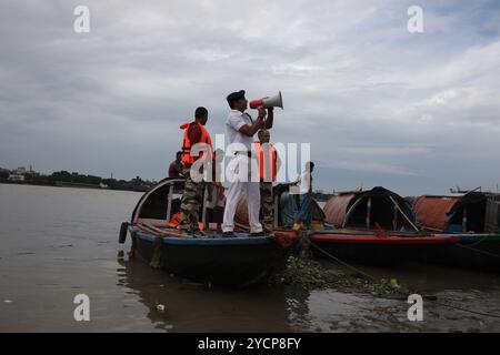 Kalkutta, Westbengalen, Indien. Oktober 2024. Ein Mitglied der Verkehrspolizei für den Fluss Kalkutta appelliert mit einem Megaphon an die Menschen, während des Benzins auf dem Fluss Ganges in Kalkutta, Indien, am 23. Oktober 2024 an einen sicheren Ort vor dem Zyklon Dana zu ziehen.das regionale Meteorologische Zentrum Kalkutta (IMD) sagte am Mittwoch voraus, dass der Sturm Dana in den nächsten drei Tagen schwere Regenfälle in mehreren Bezirken Odisha und Westbengalen bringen wird. Der Zyklon Dana wird voraussichtlich am frühen Freitag zwischen dem Bhitarkanika-Nationalpark und dem Hafen von Dhamra im Bezirk Odisha an Land kommen, wobei Windgeschwindigkeiten bis zu 120 Kilometer betragen Stockfoto