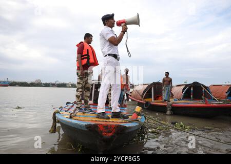 Kalkutta, Westbengalen, Indien. Oktober 2024. Ein Mitglied der Verkehrspolizei für den Fluss Kalkutta appelliert mit einem Megaphon an die Menschen, während des Benzins auf dem Fluss Ganges in Kalkutta, Indien, am 23. Oktober 2024 an einen sicheren Ort vor dem Zyklon Dana zu ziehen.das regionale Meteorologische Zentrum Kalkutta (IMD) sagte am Mittwoch voraus, dass der Sturm Dana in den nächsten drei Tagen schwere Regenfälle in mehreren Bezirken Odisha und Westbengalen bringen wird. Der Zyklon Dana wird voraussichtlich am frühen Freitag zwischen dem Bhitarkanika-Nationalpark und dem Hafen von Dhamra im Bezirk Odisha an Land kommen, wobei Windgeschwindigkeiten bis zu 120 Kilometer betragen Stockfoto