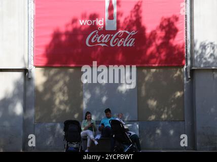 Atlanta, USA. Oktober 2024. Besucher ruhen sich am 23. Oktober 2024 im World of Coca-Cola in Atlanta, Georgia, USA, unter einem Coca-Cola-Logo aus. Die Coca-Cola-Aktien gingen am Mittwoch um fast 2 Prozent zurück, nachdem das Unternehmen im dritten Quartal ein schwächeres Stückzahlvolumen meldete. Quelle: Liu Yanan/Xinhua/Alamy Live News Stockfoto