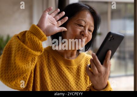 asiatische Seniorin, die auf dem Smartphone chatten und zu Hause freundlich lächeln Stockfoto