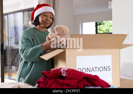 Ältere asiatische Seniorin im Weihnachtsmann hat Teddybären zu Hause in Spendenbox verpackt, Weihnachten Stockfoto