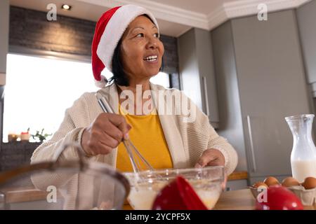 asiatische Seniorin mit Weihnachtsmütze, die zu Hause fröhlich backen während Weihnachten Stockfoto