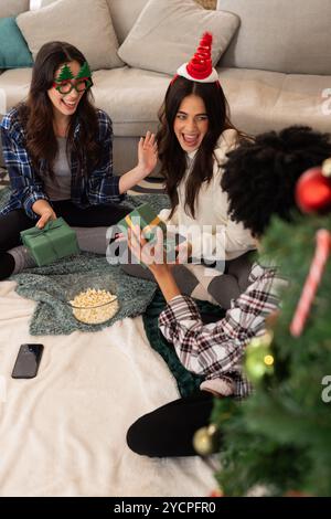 Multirassische Freundinnen tauschen Geschenke aus und lachen während der Weihnachtsfeier zu Hause Stockfoto
