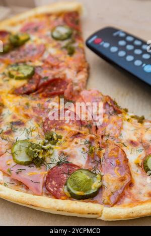 Pizzastücke in Box mit tv-Fernbedienung Stockfoto