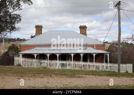 Altes, heruntergekommenes australisches Haus mit Wellblech-Dach, Veranda mit Kunstwerk und weißem Pfahlzaun in ländlicher Landschaft. Eine vergangene Ära. Stockfoto