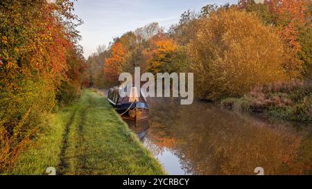 Blick auf einen Kanal und die wunderschönen Herbstfarben. Ein schmales Boot liegt am Schleppweg und es gibt Reflexionen im stillen Wasser Stockfoto