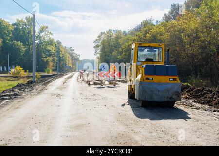 Eine gelbe Rollbahn, die auf einer teilweise fertiggestellten Straße geparkt ist. Eine Eislaufbahn zum Verlegen von Asphalt oder Sand bei Straßenreparaturen oder Bauarbeiten. Straßenreparatur Stockfoto