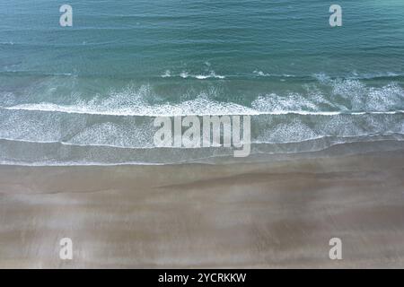 Blick von oben auf das türkisfarbene Meer und die weißen Wellen, die an einem leeren goldenen Sandstrand brechen Stockfoto