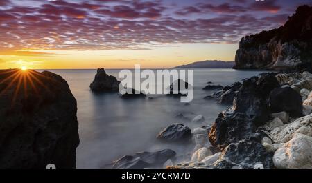 Ein farbenfroher Sonnenaufgang in Cala Gonone mit schwarz-weißen Felsen und Felsbrocken und einem Sonnenaufgang Stockfoto