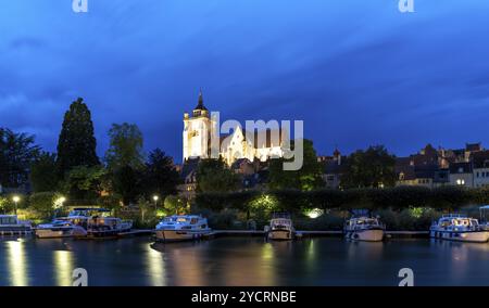 Dole, Frankreich, 14. September 2022: Nächtlicher Blick auf die beleuchtete katholische Kirche Notre Dame in Dole mit Hausbooten auf dem Doubs River im Foregr Stockfoto