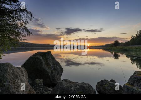 Ein farbenfroher Sonnenuntergang über einem ruhigen See mit Reflexionen im Wasser und Felsen im Vordergrund Stockfoto