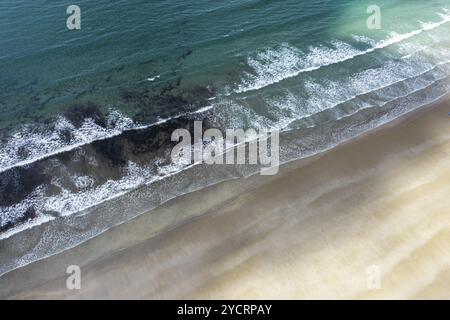 Blick von oben auf das türkisfarbene Meer und die weißen Wellen, die an einem leeren goldenen Sandstrand brechen Stockfoto