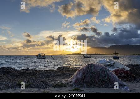 Pula, Italien, 10. Dezember 2022: Fischerboote vor Anker an der zerklüfteten Bergküste Sardiniens bei Sonnenuntergang mit Fischernetzen im Vordergrund, EUR Stockfoto