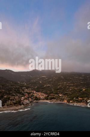 Ein Drohnenblick auf Seccheto Beach und das Dorf auf Elba Island kurz nach Sonnenuntergang mit einem nebligen lila Himmel Stockfoto