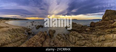 Panoramablick auf einen goldenen Sandstrand bei Sonnenuntergang mit ruhigem Meerwasser und Granitfelsen Stockfoto