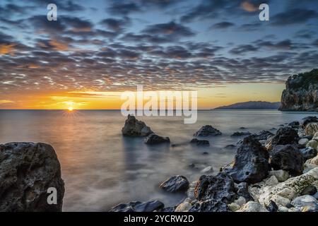 Ein farbenfroher Sonnenaufgang in Cala Gonone mit schwarz-weißen Felsen und Felsbrocken und einem Sonnenaufgang Stockfoto