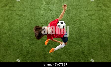 Luftaufnahme einer jungen Sportfrau, Fußballverteidigerin in bequemer Uniform, die den Ball mit der Brust in der Luft trifft. Stockfoto