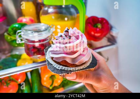 Frau nimmt den süßen Kuchen aus dem offenen Kühlschrank Stockfoto