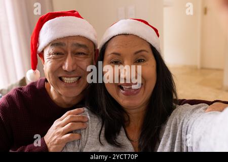 Lächelndes Seniorenpaar mit Weihnachtsmützen und Selfie zu Hause während Weihnachten Stockfoto