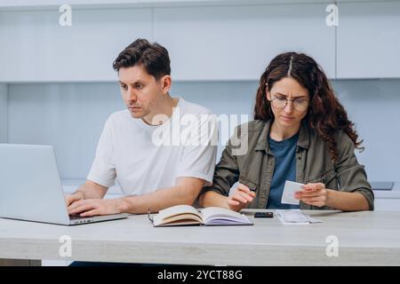 Das junge Paar sitzt an ihrem Küchentisch, verwaltet gemeinsam ihre Finanzen und sieht besorgt aus, während es Rechnungen und Kontoauszüge überprüft Stockfoto