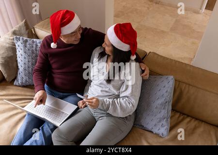 Weihnachtszeit, Seniorenpaar mit weihnachtsmützen, die online mit Laptop einkaufen Stockfoto