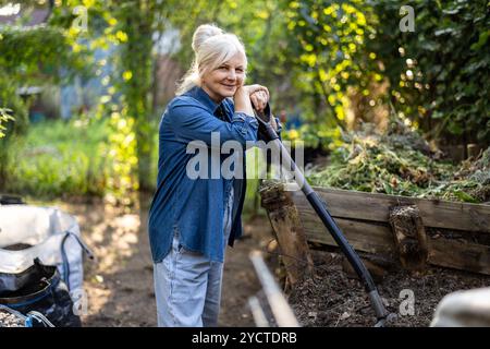 Eine ältere Frau schaufelt Komposthaufen in ihrem Garten Stockfoto