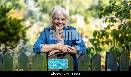 Frau, die sich auf einen Holzzaun lehnt, mit dem Schild „Welcome to my Garden“ Stockfoto