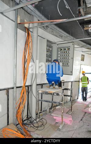 Ein Elektriker führt Verdrahtungsaufgaben an einem Verteiler auf einer aktiven Baustelle durch. Stockfoto