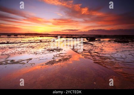 Sonnenaufgangshimmel reflektiert sich bei Ebbe auf den freiliegenden Felsen Stockfoto