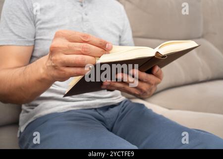 Nahaufnahme eines Handmannes, der ein Papierbuch liest und zu Hause auf einem Sofa sitzt Stockfoto