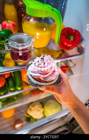 Frau nimmt den süßen Kuchen aus dem offenen Kühlschrank Stockfoto