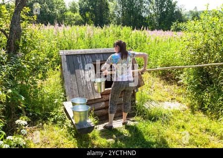 Junge attraktive Frau nahe am Dorf aus Holz Wasser gut in sonnigen Sommertag Stockfoto