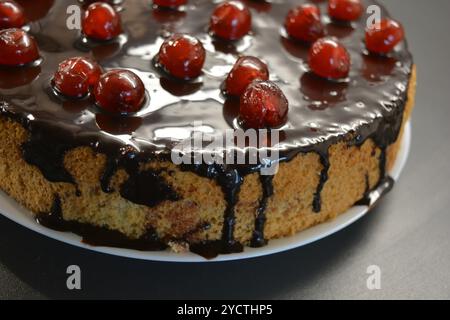 Kuchen mit eigenen Händen zubereitet. Weißer Biskuitkuchen „Drunken Cherry“, dekoriert mit Schokoladenglasur mit karamellisierten, roten und hellen, süßen Kirschen. Stockfoto