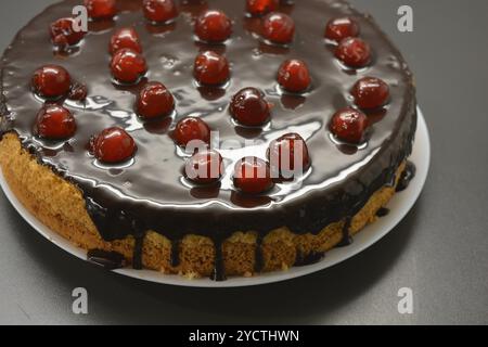 Kuchen mit eigenen Händen zubereitet. Weißer Biskuitkuchen „Drunken Cherry“, dekoriert mit Schokoladenglasur mit karamellisierten, roten und hellen, süßen Kirschen. Stockfoto