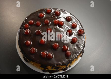Kuchen mit eigenen Händen zubereitet. Weißer Biskuitkuchen „Drunken Cherry“, dekoriert mit Schokoladenglasur mit karamellisierten, roten und hellen, süßen Kirschen. Stockfoto